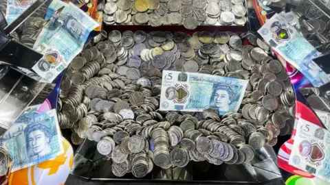 Getty Images An arcade machine. It is full of silver coins and bank notes. 