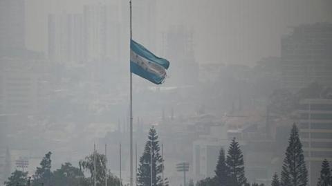 A Honduran national flag flies amidst a dense layer of smoke covering Tegucigalpa.