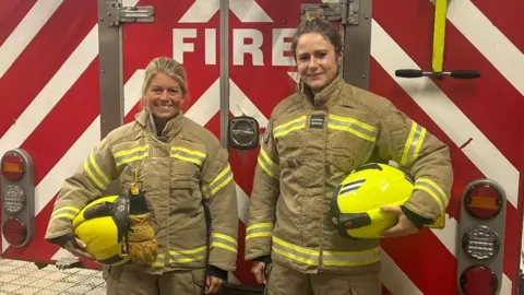 Jordie O’Hara and Katie Gray standing side-by-side in their firefighting kit in front of a fire engine.