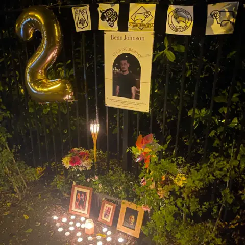 Supplied A memorial beside a metal fence with framed photographs, flowers, candles and a large balloon in the shape of the number two.
