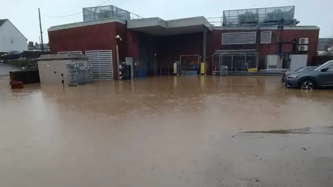 Flooded car park behind a large red brick building.