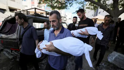 Reuters Mourners carry the bodies of two Palestinian children reportedly killed in an Israeli strike, during a funeral at al-Shifa Hospital, in Gaza City (6 July 2025)