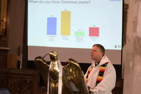 PA Rev Andrew Beane in front of a screen showing the results of a congregation vote during a service at Aylsham Parish Church in Norfolk