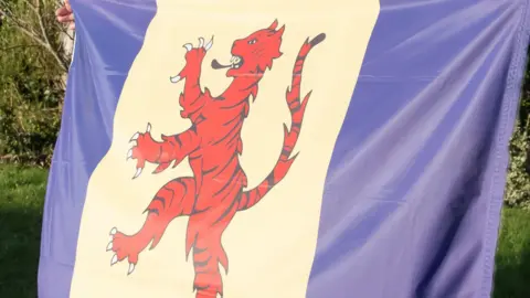 Close-up view of the Fenland flag. The flag has two vertical strips of blue at each end of the flag, separated by a strip of white in the centre. On the white strip is an image of a tiger.