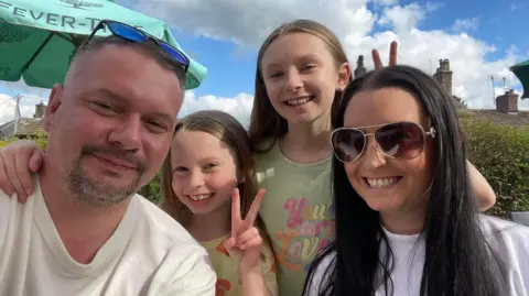 Family handout Group family picture of Natalia and her older sister with theirdad and mum. The girls are in the centre smiling and holding up their hands in peace signs. They are at an outdoor cafe.