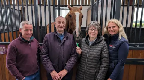 BBC Bloodstock agent Tom Malone (L), Native River's owners Garth and Anne Broom, and the former racehorse's trainer Emma Vine (R) standing in front of Native River's pen