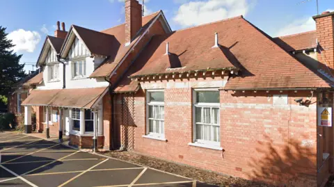 Google A large early 20th Century brick building with a two storey centre section and single storey wings
