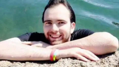 Family Handout A smiling Ryan Carter on a sunny day by a body of water. He appears to have been swimming as his hair appears wet.