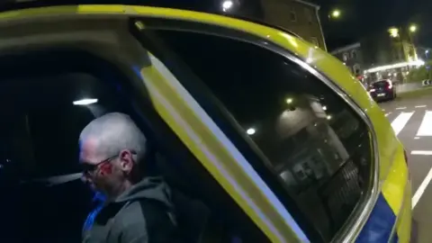 Kent Police A man with a shaved head is sitting in the back of a police car.