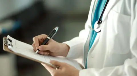 A Doctor in a white coat writing on clipboard with a black pen. Only the dr's torso can be seen. 