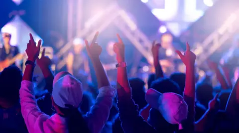 The back of young people's heads can be seen, with their arms raised in the air. 