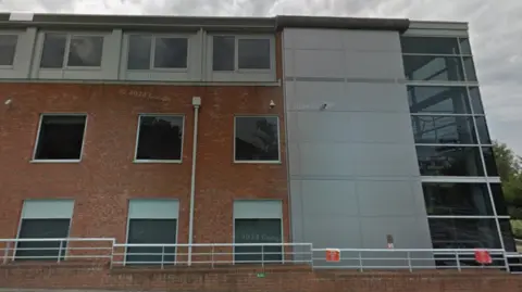 Google A three storey brick building with dark glass windows.