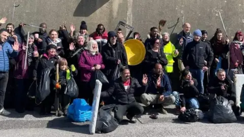 Stand Up to Racism Dorset Migrants from the Bibby Stockholm and local people posing with full bin bags following a beach litter clean