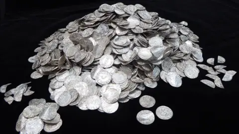 PA Media A hoard of stacked silver coins displayed in front of a black background.