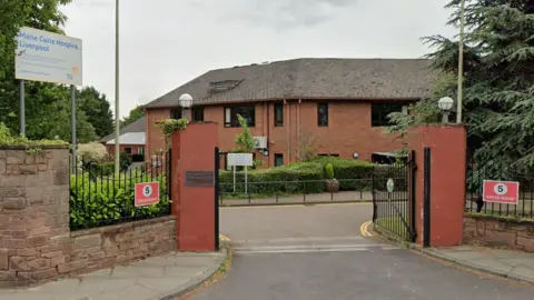 Google A red brick building set behind a sandstone entrance and green trees and bushes