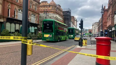 Police tape at the scene of the bus crash in Leeds. Two stationary buses and a police car can be seen in the photo.