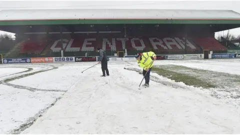 Pacemaker People attempt to clear snow from the Oval football ground