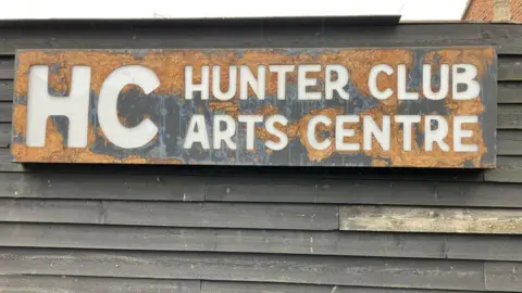 A large sign on a wall made up of wooden panels which reads HC Hunter Club Arts Centre