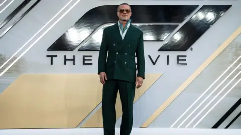 Jeff Spicer/Getty Images for Warner Bros. Pictures Brad Pitt in front of the F1: The Movie logo at the European Premiere at Cineworld Leicester Square on 13 June 2025 in London. He is wearing a dark green suit.