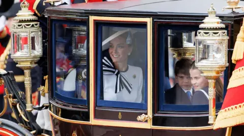  EPA-EFE/REX/Shutterstock Catherine smiling as she looks through gold carriage window, alongside Louis and Charlotte
