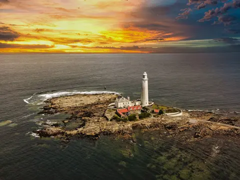 David Dodds A lighthouse on a rocky outcrop with a sunrise in the background