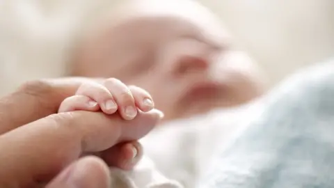 Getty Images Stock image of a person holding a newborn baby's hand