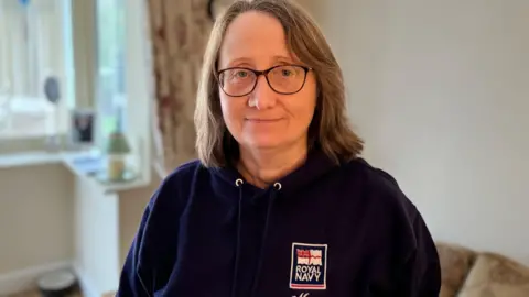 A woman in a blue jumper standing in a living room 