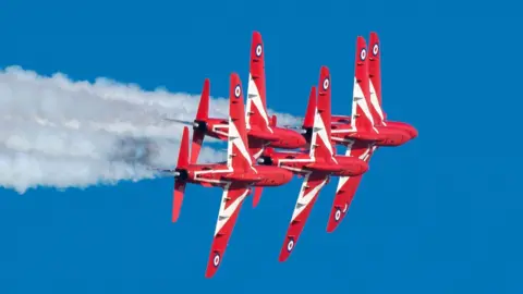 Five bright red jet planes fly together in a tight formation. 