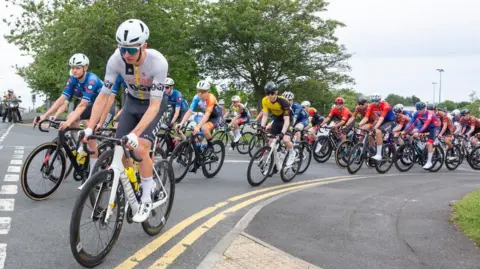 Dozens of male cyclists in helmets and cycling gear turning at a junction during Consett Cycle Festival on 22 June 2025.