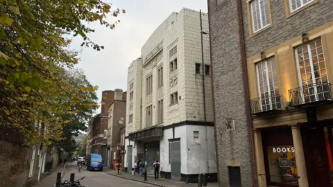Steve Hubbard/BBC Hobson Street, with the former cinema on the right-hand side. You can see the building's art deco facade but the brickwork is discoloured and the front doors and windows are boarded up. Next to it is a bookshop.