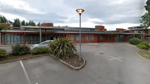 Google Google street view picture of the outside of the care home. It is a low building, built with red bricks and a grey roof. Picture taken from the adjoining car park.