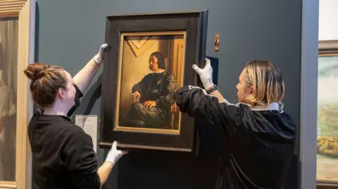 Museum workers placing artwork on a wall.