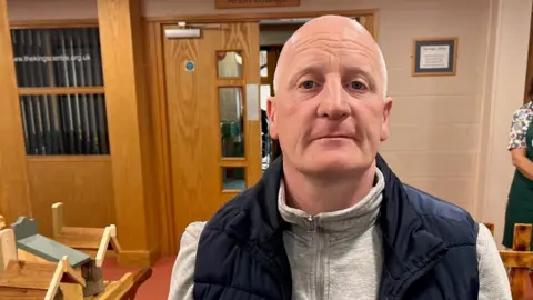 Image of Gary Woodcock, wearing a blue gilet and grey jumper, in the foodbank.