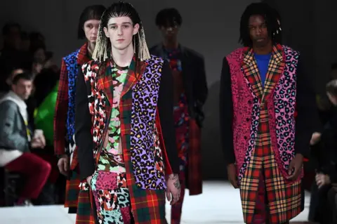 ANNE-CHRISTINE POUJOULAT/Getty Models in brightly coloured outfits and corn-rows walking down the cat walk
