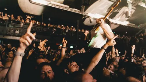 A concert at Nottingham's Rock City, where a guitarist has walked into the packed audience and is being held up by them