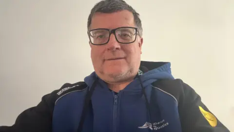 Andy Moore A man wearing glasses taking a selfie, in a blue and black zip up jumper which says Southwark Aquatics.