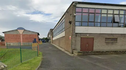 An old school building in the Borders with many windows and brick walls and tarmac around it
