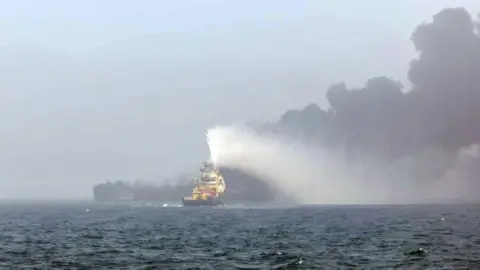 PA Media A firefighting ship dousing a burning oil tanker with water at sea