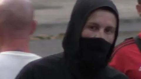 Avon and Somerset Police A man with his hood up and a face covering. 