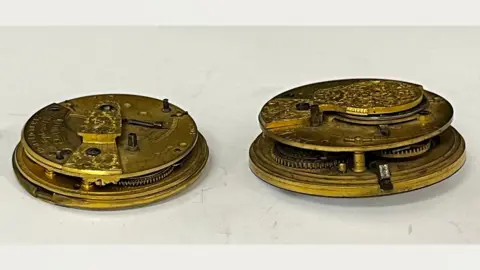 TW Gaze Side views of two mid-19th Century gold-coloured watch movements. The one on the right is slightly smaller than the one on the left. The views reveal each has two discs, one laid over the other with just glimpsed wheels in between.