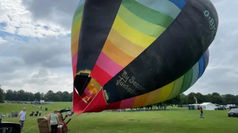 Sam Read/BBC Rainbow-coloured balloon inflates and starts to lift off the ground at the Racecourse.  