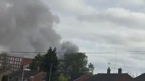 JOANNE ASHMAN A large quantity of black smoke can be seen above the tops of houses, trees and a hotel in Cambridge. It is cloudy, with some pockets of blue sky.