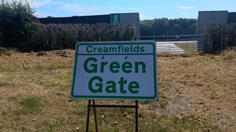 A Creamfields Green Gate sign on grass by the main road by the site