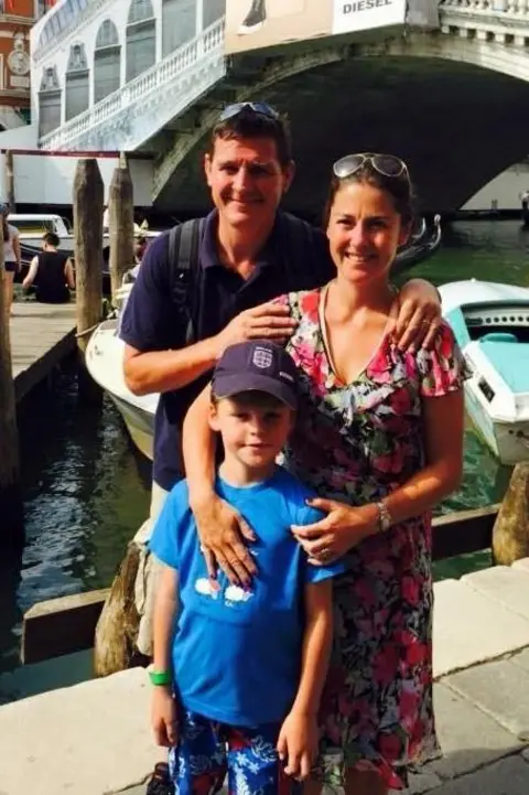 Anna-Louise Bates A man and woman are standing with a young boy in Venice, with a gondola behind them. They are all smiling.
