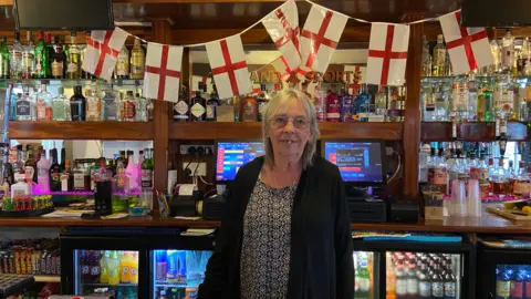 BBC/Emily Coady-Stemp Carol Coomber behind the bar in the social club