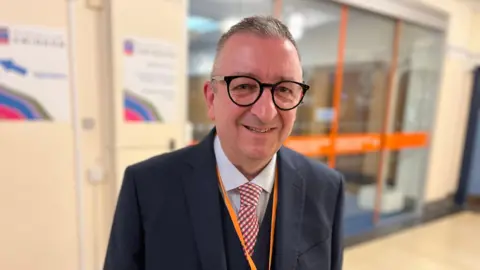 Councillor Gary Sumner smiles at the camera, wearing a suit, tie and glasses.