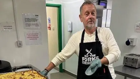 Julian Trust A man wearing a chef's apron stands over a tray of food he has made at the Julian Trust in Bristol