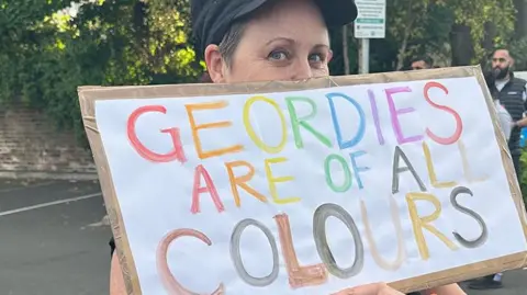 A woman holds a sign saying 'Geordies are of all colours'.