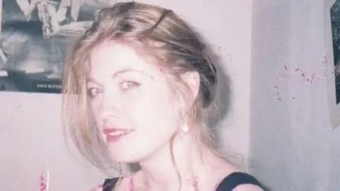 University of Bristol A photograph of a woman with blonde hair, looking into the camera. Posters can be seen in the background behind her.