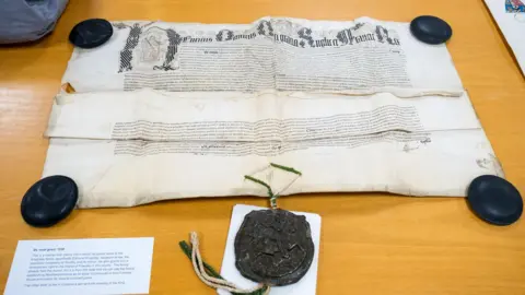 West Northamptonshire Council A document granting land is displayed on a table, with weights at each corner. A seal is at the front of the picture.